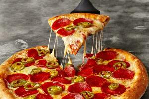 detailopname van plak van pizza met gesmolten kaas, peperoni en jalapeno Aan portie spatel foto