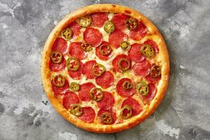 pittig dun pizza met gesmolten Mozzarella, peperoni en jalapeno Aan grijs steen achtergrond foto