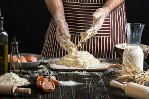 tegen de achtergrond van Mannen handen kneden de deeg. ingrediënten voor Koken meel producten of deeg brood, muffins, taart, pizza deeg . foto