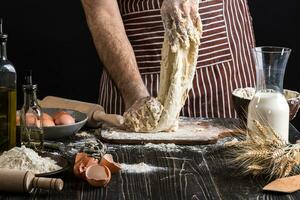 tegen de achtergrond van Mannen handen kneden de deeg. ingrediënten voor Koken meel producten of deeg brood, muffins, taart, pizza deeg . foto