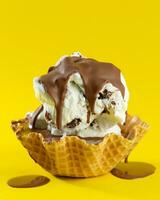 ijs room met chocola en noten in wafel ijshoorntje Aan geel achtergrond foto