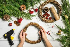 Kerstmis handgemaakt diy achtergrond. maken ambacht Kerstmis krans en ornamenten. top visie van wit houten tafel met vrouw handen. foto