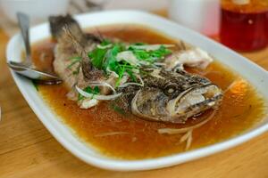 stoom- gebakken gemarmerd goby vis gebeld ikan mala's in Siamees stijl geserveerd in een schotel Aan een houten tafel in een restaurant in Indonesië foto