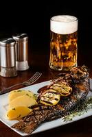 gegrild karper vis met rozemarijn aardappelen, citroen en bier Aan een houten tafel. zwart achtergrond. foto