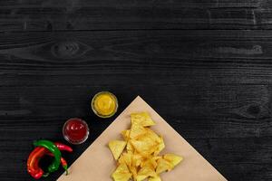 top visie van tortilla chips met saus en rood Chili peper Aan zwart houten achtergrond foto