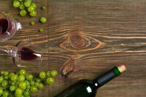twee bril, fles van rood wijn en druif Aan een houten tafel foto
