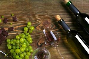 flessen en bril van wijn, chocola en rijp druiven Aan houten achtergrond foto