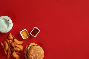 concept van bespotten omhoog hamburger, aardappelen, saus en drinken Aan rood achtergrond. kopiëren ruimte voor tekst en logo. foto