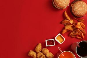 snel voedsel schotel top visie. vlees hamburger, aardappel chips en glas van drinken Aan rood achtergrond. meenemen samenstelling. foto