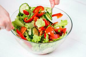 jong vrouw dressing groente salade met olijf- olie Aan een wit achtergrond foto