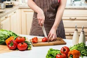 jong vrouw Koken in de keuken Bij huis. een vrouw bezuinigingen een tomaat en groenten met een mes. foto