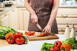 jong vrouw Koken in de keuken Bij huis. een vrouw bezuinigingen een tomaat en groenten met een mes. foto