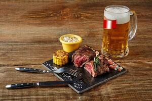 gegrild lende steak rosbief en champignons saus Aan zwart snijdend bord en glas van bier Aan houten achtergrond foto