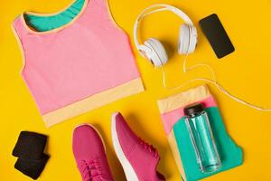geschiktheid accessoires Aan een geel achtergrond. sportschoenen, fles van water, oortelefoons en sport top. foto