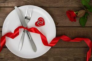 valentijnsdag dag tafel instelling met bord, vork, mes, rood hart, ring, lint en roos. achtergrond foto