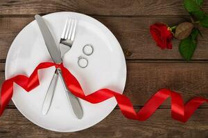 valentijnsdag dag tafel instelling met bord, vork, mes, ring, lint en roos. achtergrond foto