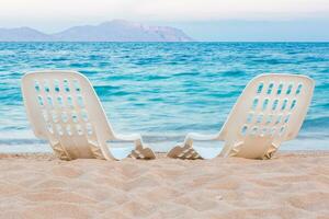 landschap van twee eenzaam strandstoelen Aan de zand in de buurt zee foto