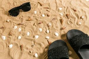 zwart slippers en zonnebril, zeeschelp Aan zand. met plaats voor uw tekst. top visie foto