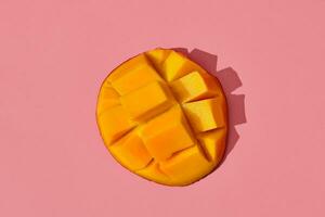 kleurrijk fruit patroon van vers sappig gesneden mango houdende Aan de midden- van de beeld Aan koraal roze achtergrond, top visie foto