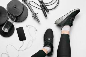 vrouwen poten in sportschoenen, geschiktheid kleding, smartphone, halters, koptelefoon, top visie. foto