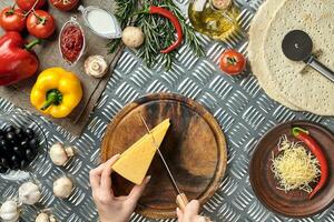 gedeeltelijk visie van vrouw snijdend kaas terwijl Koken eigengemaakt Italiaans pizza foto