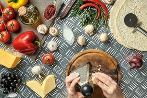 vrouw handen gewreven kaas geraspt Aan pizza, ingrediënten voor Koken pizza Aan metaal tafel, top visie foto