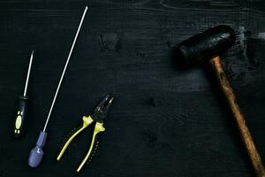 schroevendraaiers, hamer, tang en gereedschap Aan een zwart houten tafel. top visie foto