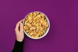 vrouw handen Holding kom met gezond ontbijt, detailopname. kom met cornflakes Aan de kleurrijk achtergrond foto