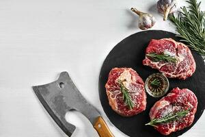 vers rauw rundvlees steaks met kruiden, knoflook, olijf- olie, peper, zout en rozemarijn Aan zwart bord lende, lendenstuk, rib oog foto