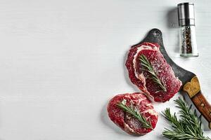 twee vers rauw steaks met kruiden, knoflook, olijf- olie, peper, zout, rozemarijn en een keuken bijl Aan wit achtergrond. top visie. foto