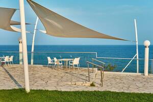 restaurant terras van een hotel met wit tafels en stoelen. zee kust, wit steen kaap in kalymnos eiland of gouverneur strand in Cyprus. foto