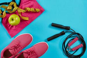 vlak leggen van vrouw sport uitrustingen in roze kleur met springen touw en sportschoenen Aan blauw achtergrond foto