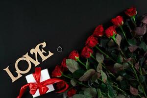 rood rozen, ring en geschenk doos Aan zwart achtergrond foto