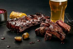 varkensvlees ribben in barbecue saus en een glas van bier Aan een zwart leisteen gerecht. een Super goed tussendoortje naar bier Aan een donker steen achtergrond. top visie met kopiëren ruimte foto