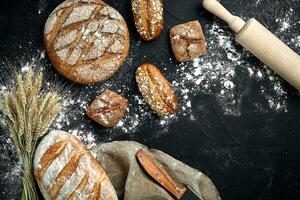 eigengemaakt rogge brood besprenkeld met meel en divers granen en zaden Aan een zwart achtergrond met aartjes van tarwe of rogge en haver. foto