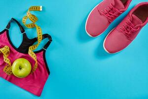 sportschoenen met meten plakband Aan cyaan blauw achtergrond. centimeter in geel kleur, roze sportschoenen, vrouw sport top en appel, kopiëren ruimte. foto