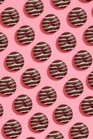 voedsel ontwerp met smakelijk chocola geglazuurd donut met wit stroken Aan koraal roze pastel achtergrond top visie patroon foto