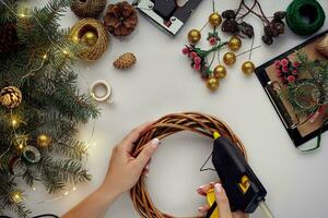 vrouw handen versieren de Kerstmis krans met net takken met een rood BES en Woud kegels. wit achtergrond. nieuw jaar concept. foto