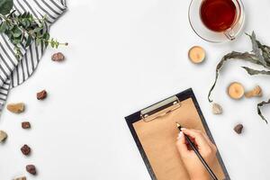 een vrouw handen schrijven Aan leeg boek Opmerking, dagboek, verspreiding model, top visie, studio. kop van thee pauze. foto