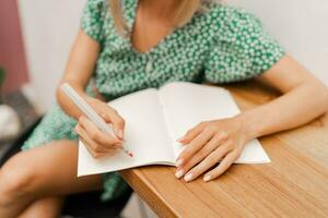 mooi blond vrouw schrijven in notebook. vervelend zomer jurk. zittend in modern cafe met wit muren. foto