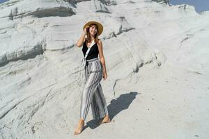 op reis vrouw in rietje hoed poseren over- wit steen landschap Aan delkikli koy in Egeïsch zee. vol lengte. foto