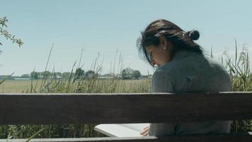 vrouw zittend op een houten bankje in het land een boek lezen foto