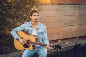 jonge man die gitaar speelt in de stad op de achtergrond van zonnestralen foto