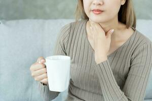 Aziatisch vrouw zetten haar hand- Aan haar nek ten gevolge naar een zeer keel. vrouw tonsillitis oorzaken een ontsteking. behandeld door nemen water, nemen antibiotica, raadplegen een dokter, virus, corona virus, influenza, griep foto