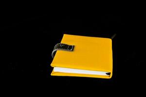 een geel notitieboekje met een zwart Hoes Aan een zwart achtergrond foto