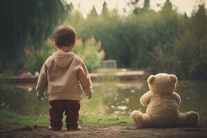 schattig weinig jongen met teddy beer in de park Bij zonsondergang, achterzijde visie van babysitten kleuter naast zijn teddy beer, ai gegenereerd foto