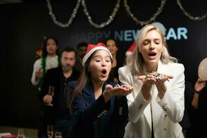 nieuw jaar partij, groep van jong mensen in de kerstman hoeden blazen confetti terwijl vieren nieuw jaar foto