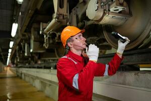 elektrisch trein ingenieur gebruik een walkietalkie naar inspecteren elektrisch trein machinerie volgens naar inspectie ronde na de elektrisch trein is geparkeerd in de elektrisch trein reparatie winkel foto