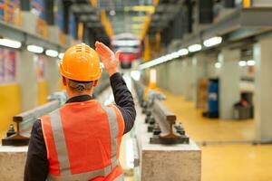 achterzijde visie van elektrisch trein industrie ingenieur vervelend een veiligheid helm en reflecterende hesje. Daar is een elektrisch auto in de auto reparatie fabriek net zo de achtergrond afbeelding. foto