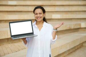 zelfverzekerd vrouw verkoop manager glimlachen op zoek Bij camera, Holding laptop met wit mockup digitaal scherm. kopiëren advertentie ruimte foto